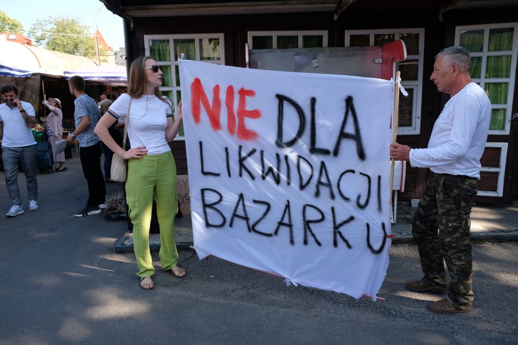 Kobieta i mężczyzna z banerem protestują przeciw likwidacji bazaru na placu Balcerowicza w Rzeszowie na tel bud