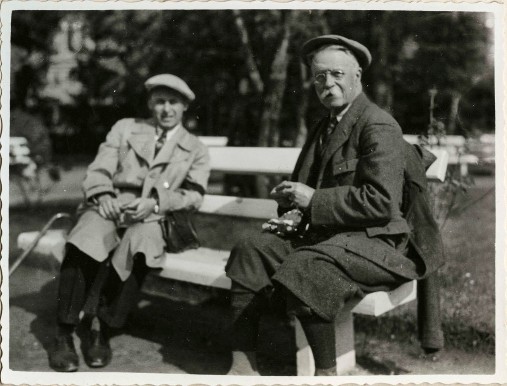Na zdjęciu znajduje się dwóch mężczyzn siedzących na ławce w parku. Jeden z nich to książę Andrzej Lubomirski