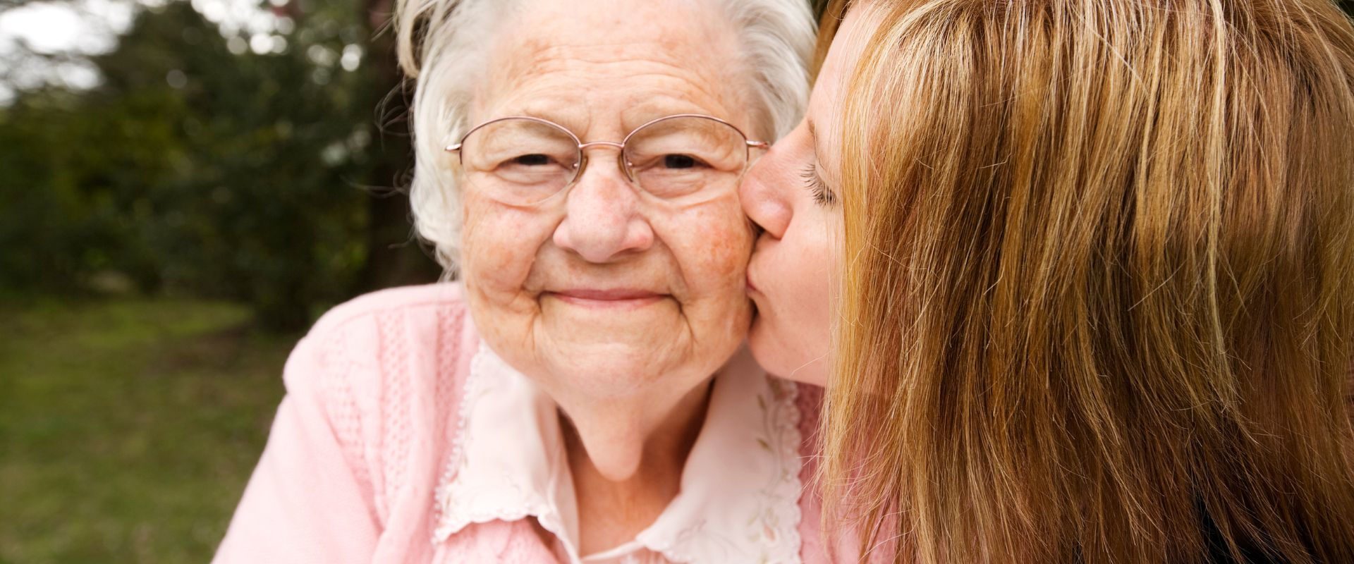 Młoda dziewczyna całuje w policzek seniorkę